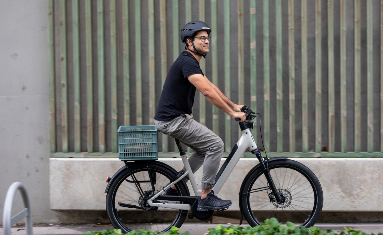 Man riding a Moustache Mardi 27.4 E-Bike  with a basket against a wooden fence.