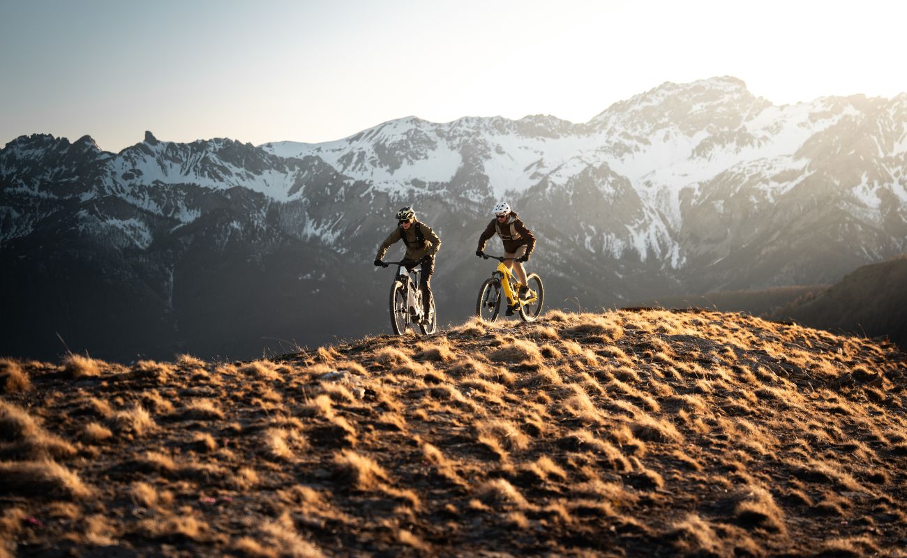 Two Orbea eMTB riders on alpine mountain trail with snow-covered peaks