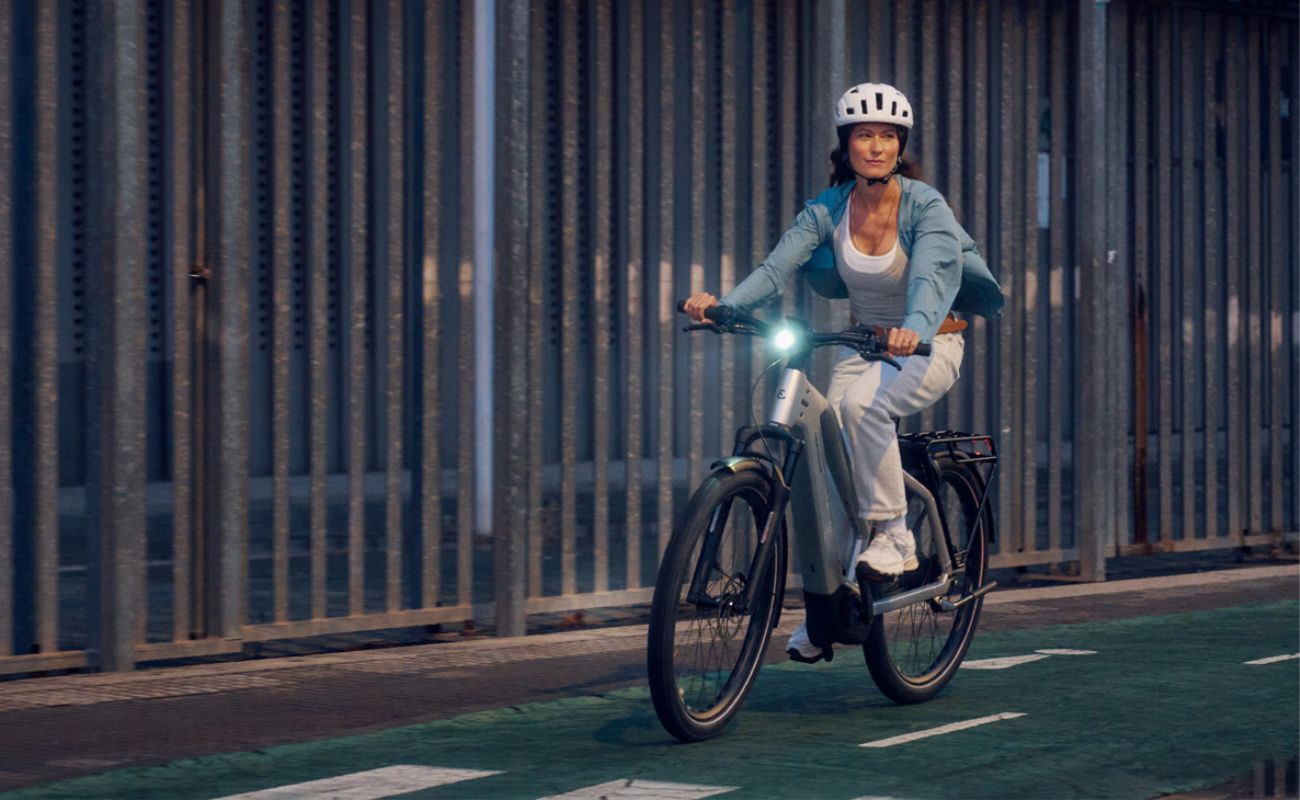 A woman riding a Riese & Muller Charger5 Mixte electric bicycle on a green bike lane at dusk