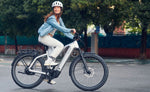 A woman riding a Riese & Muller Charger5 Mixte electric bicycle on a paved path outdoors.