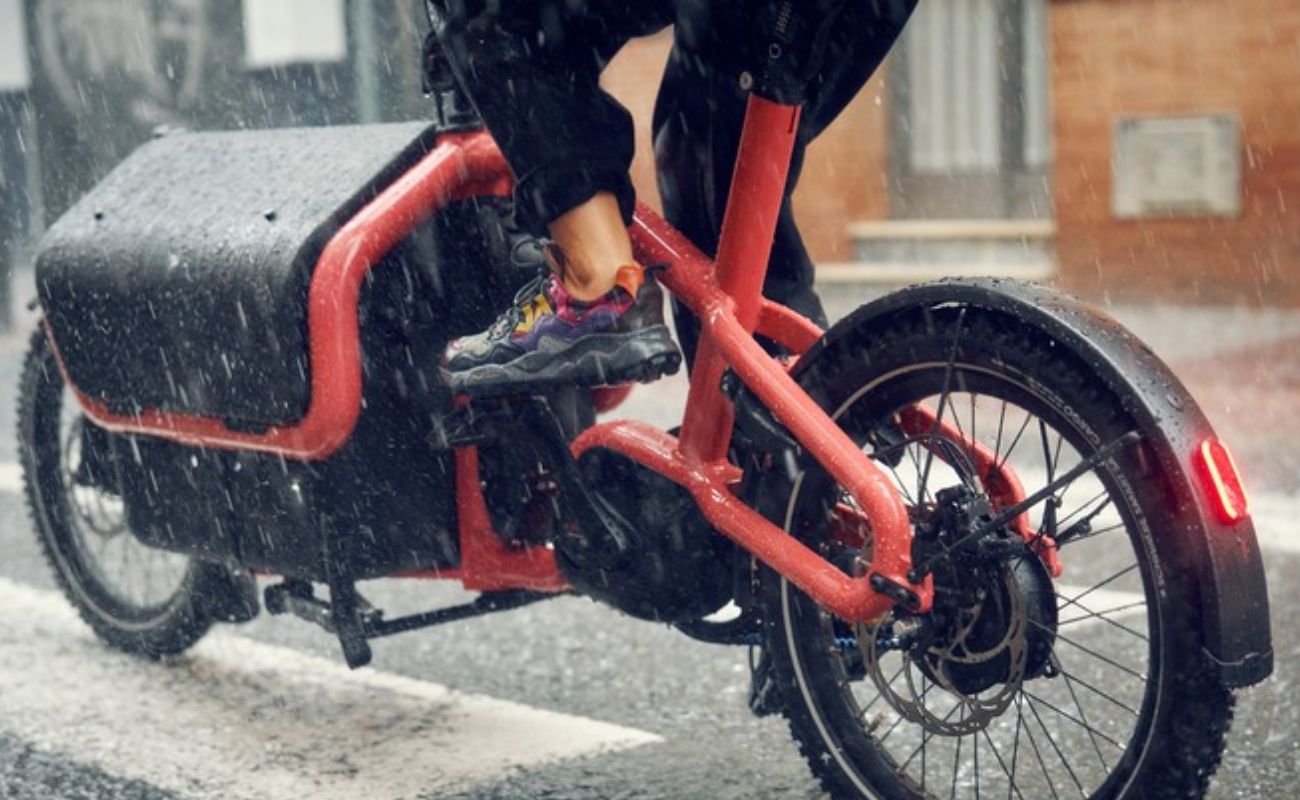 Riese & Müller Carrie2 FAMILY Coral electric cargo bike ridden in rain, showing belt drive and rear disc brake