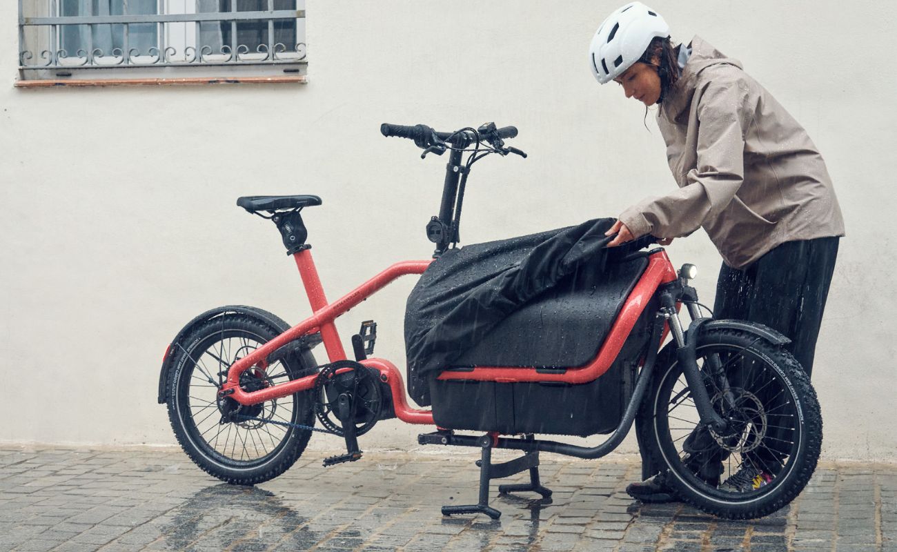 Rider adjusting the front cargo box cover on a Coral Riese & Müller Carrie2 FAMILY electric cargo bike in rain