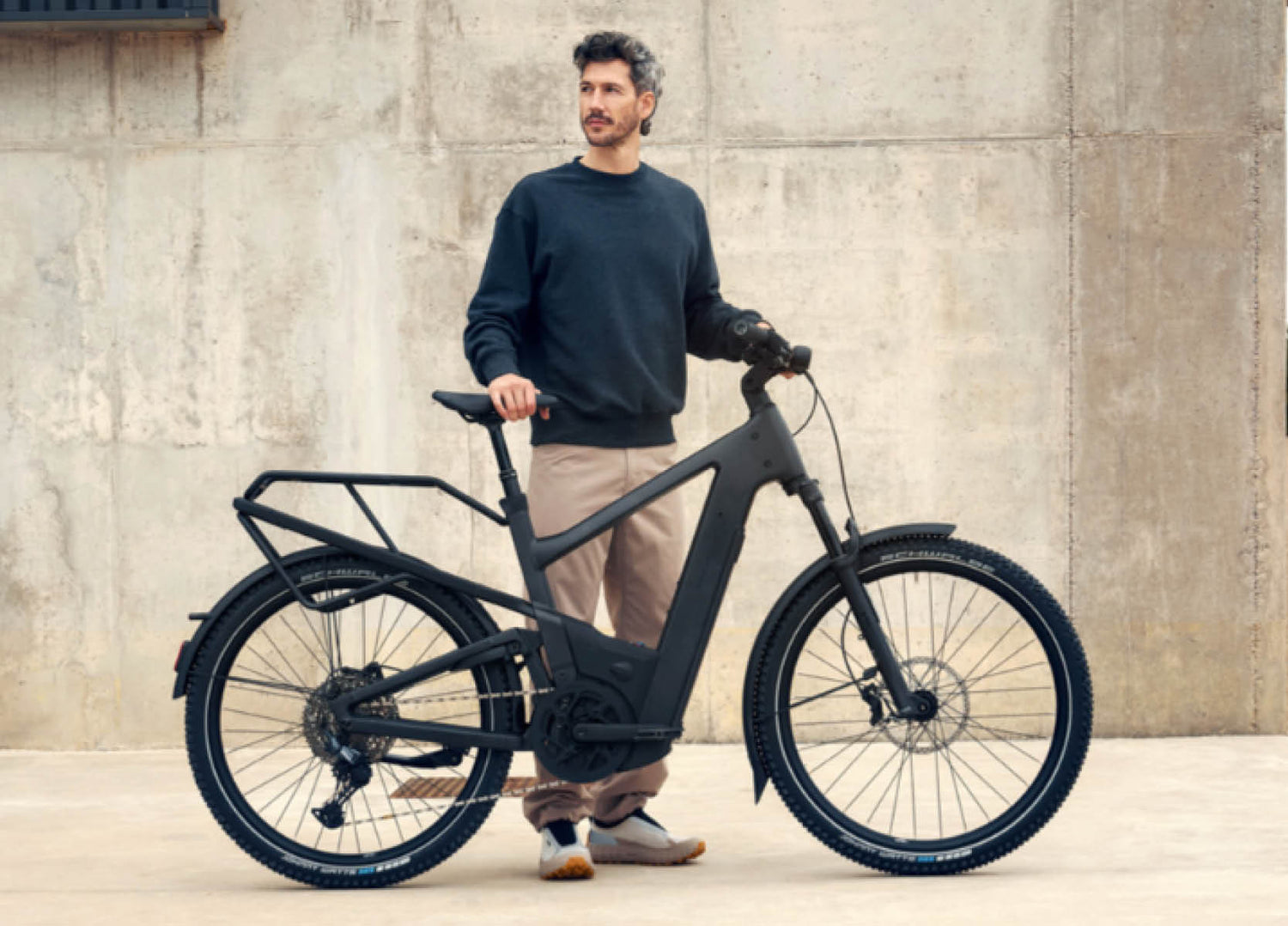 Man holding a stone grey Delite5 electric bike against a concrete wall.