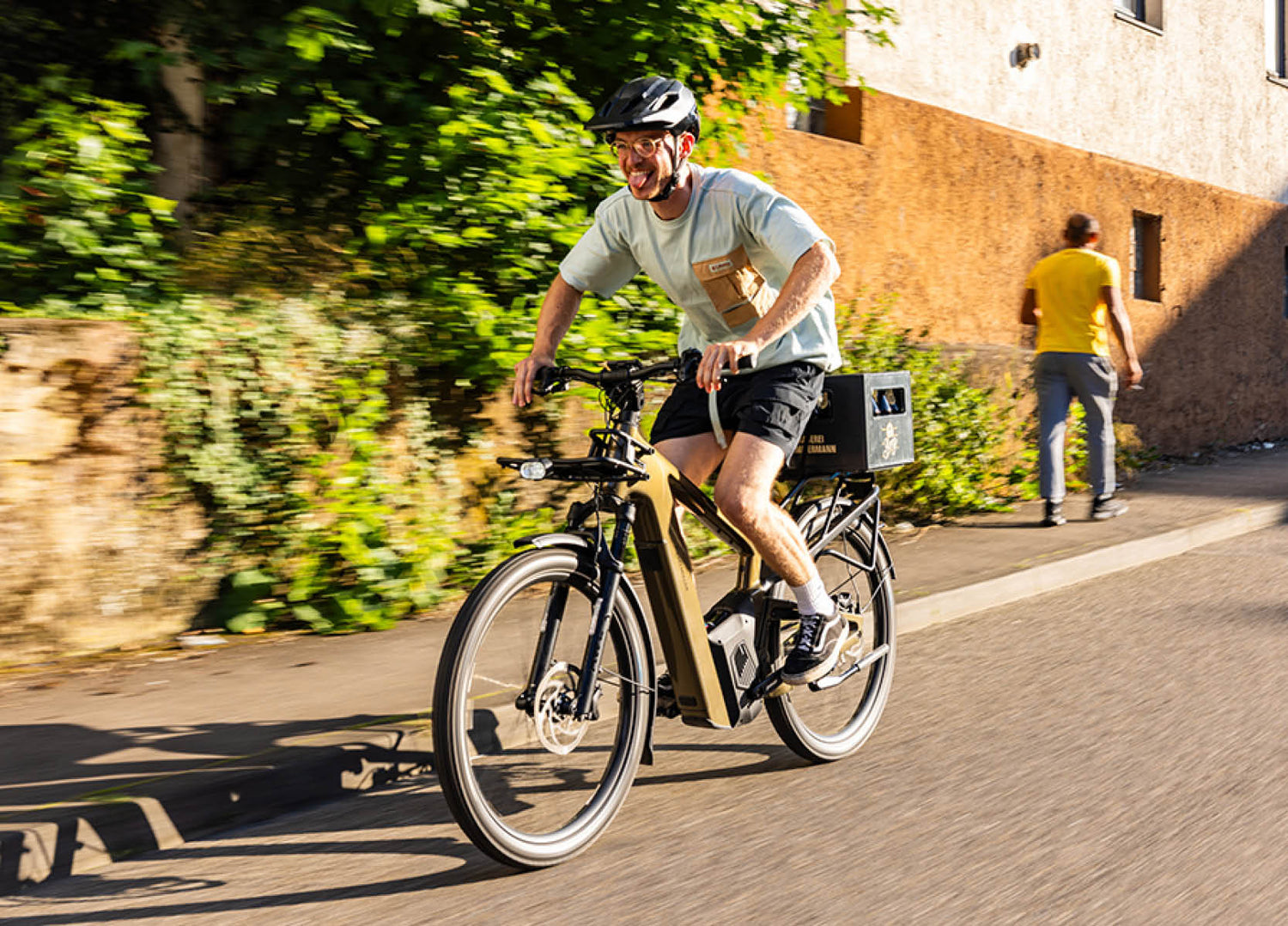 Man riding an  amber Riese & Muller Delite5 electric bike on a street with greenery and a building in the background