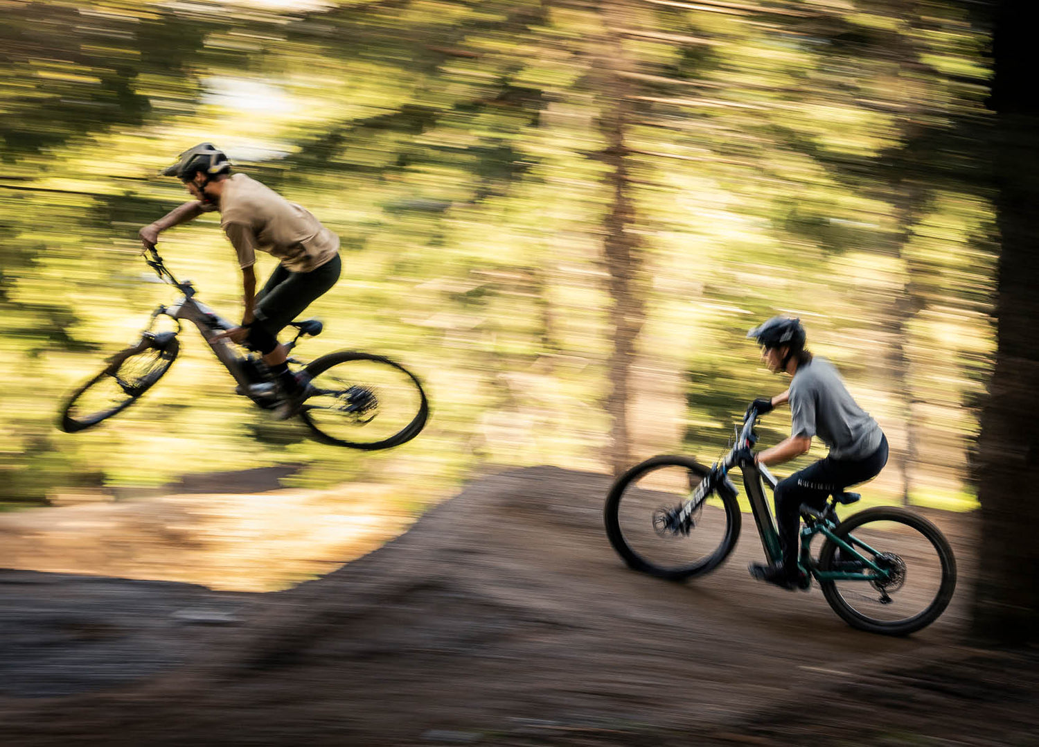 Two people jumping Focus Jam2 EMTB's on a forest trail 