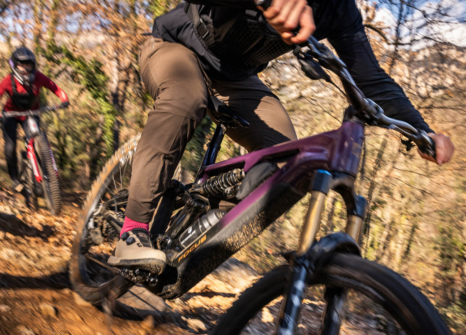 Two mountain bikers riding on Focus Sam2 EMTB's on a trail with one in the foreground and another slightly blurred in the background.