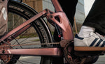Close-up of a Focus Aventura2 FS 6.8 Wa E-Bike - Nepalsilver chain and gear system with a person wearing white sneakers with blue stripes. | Electric Bikes Brisbane