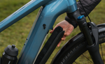 Close-up of a person adjusting the battery on a Focus F26 Aventura2 6.8 800Wh E-Bike with a blurred grass background