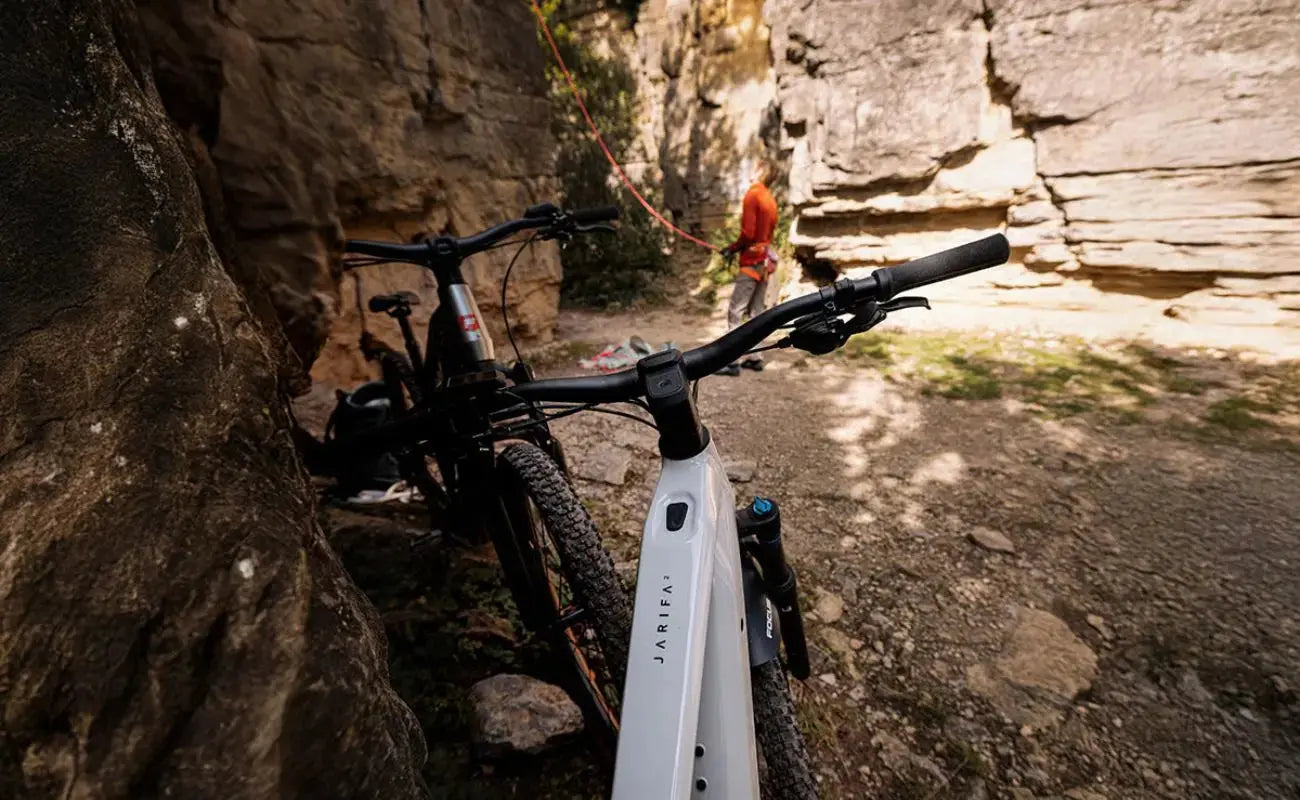 Focus F26 Jarifa2 6.7 Hardtail E-MTB, Silver leaning against a rock wall with a person in the background on a trail. | Electric Bikes Brisbane