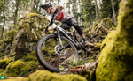 Person riding a Focus F26 Jam2 6.0 EMTB through a forest with rocks and trees.