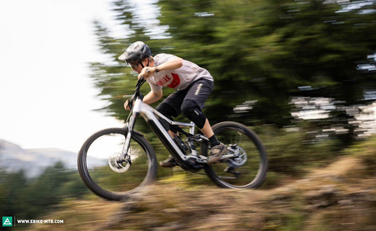 Person riding a Focus F26 Jam2 6.0 EMTB on a trail with trees in the background