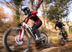 Two mountain bikers riding Focus Sam2 EMTB's through a forest on a sunny day.