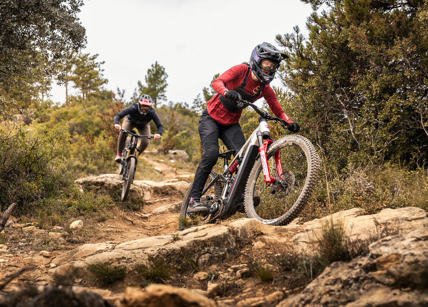 Two mountain bikers riding on Focus Sam2 eMTB's on a rocky trail in a forested area.