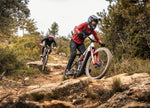 Two mountain bikers riding on Focus Sam2 eMTB's on a rocky trail in a forested area.