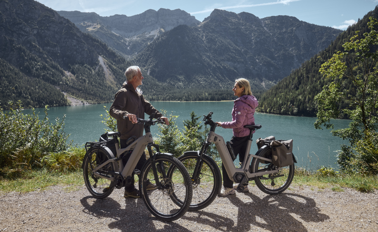 Two people with Kalkhoff K26 Entice 3 Excite Belt standing by a lake with mountains in the background | Electric Bikes Brisbane