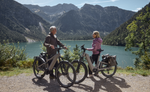 Two people with Kalkhoff K26 Entice 3 Excite Belt standing by a lake with mountains in the background | Electric Bikes Brisbane