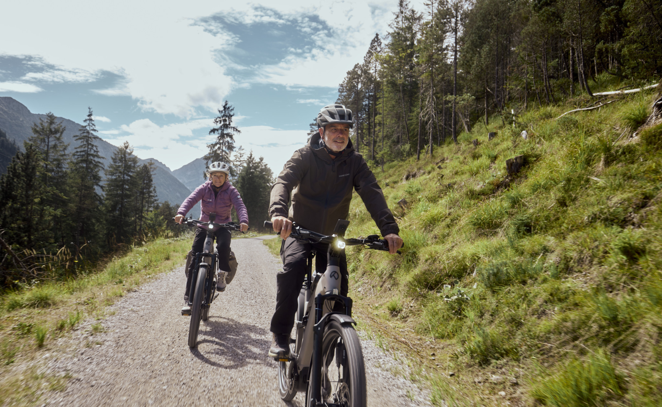 Two people riding Kalkhoff K26 Entice 3 Excite Belt on a trail with mountains and trees in the background | Electric Bikes Brisbane