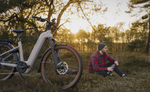 Man sitting next to a Kalkhoff K26 Entice 5+ Move Wave EBike, Moonstonegrey in a field with trees and sunset in the background