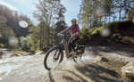 Person riding a Kalkhoff K26 Entice 5+ Move Wave EBike, Moonstonegrey through a stream in a forest with trees and rocks in the background