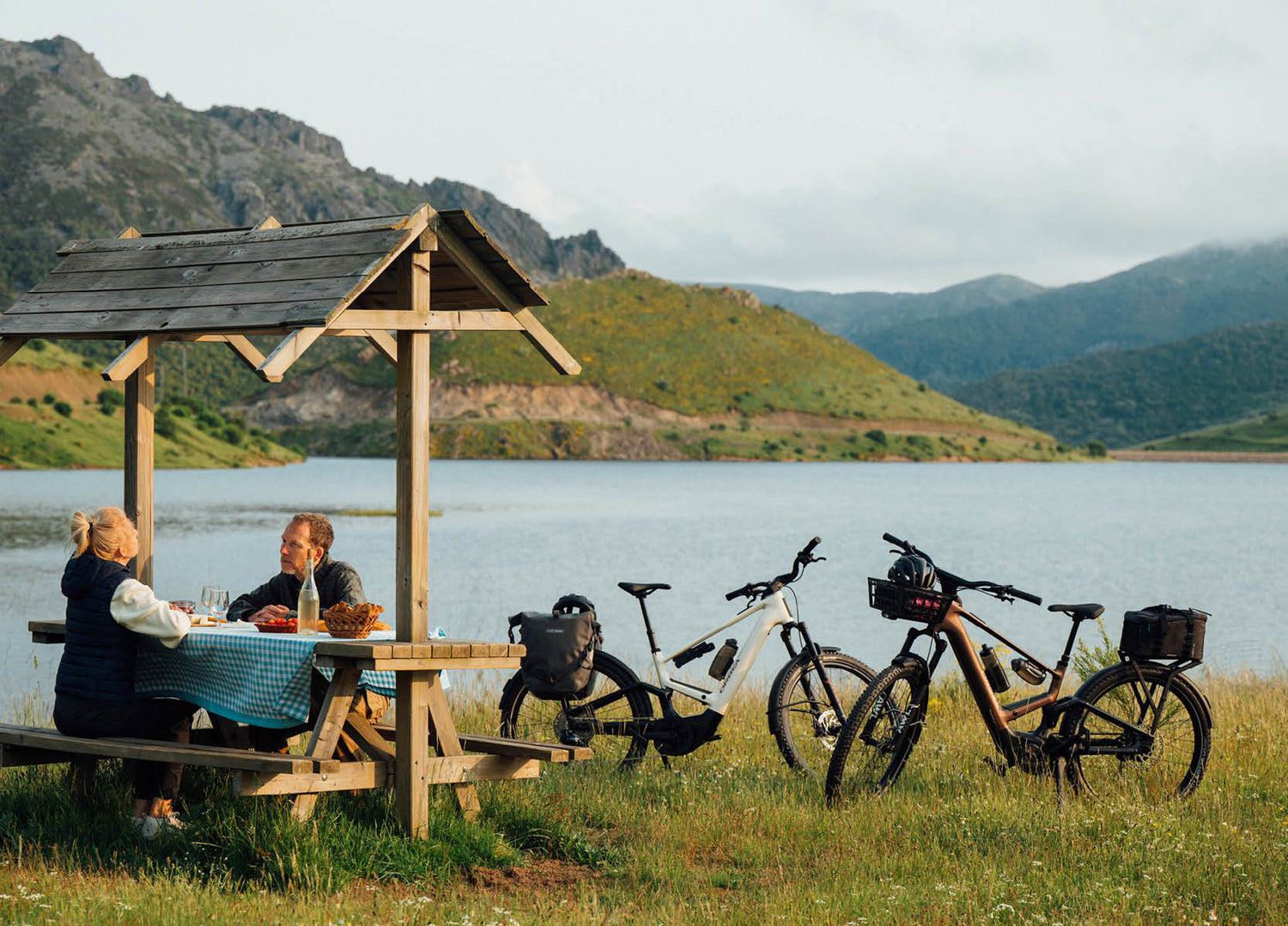 Two people sitting at a picnic table near a lake having carried their picnic on their Orbea Muga electric bikes