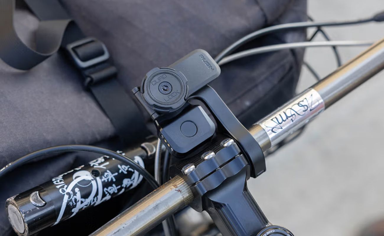 Quad Lock Bike Alarm and Finder fitted beneath a Quad Lock phone mount on a bicycle handlebar.
