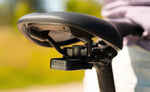 Close-up of the Quad Lock Bike Alarm and Finder mounted beneath a black bicycle saddle using a saddle rail adaptor.