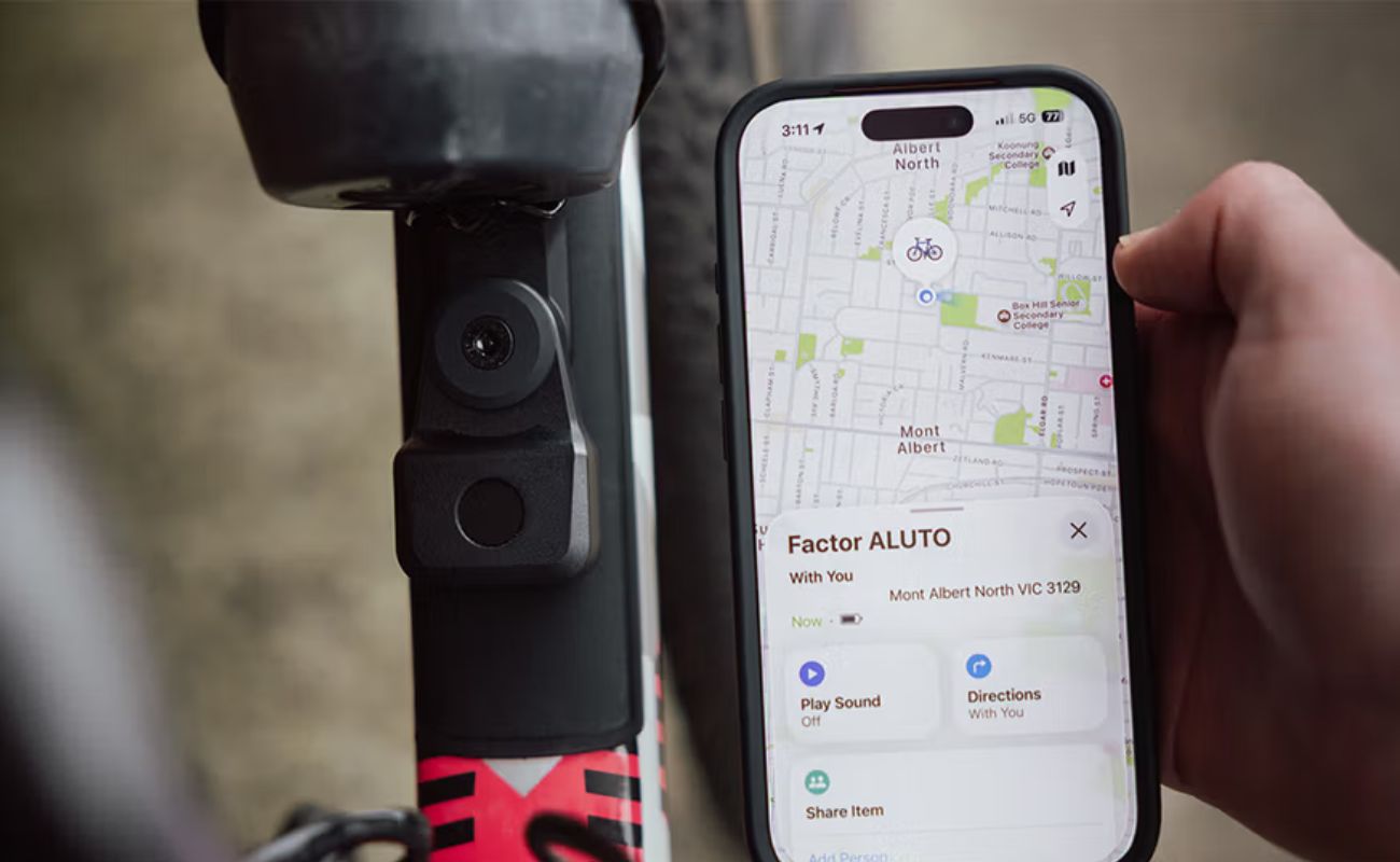 Quad Lock Bike Alarm and Finder mounted on a bike frame beside a phone displaying the bike’s location in the Find My app.