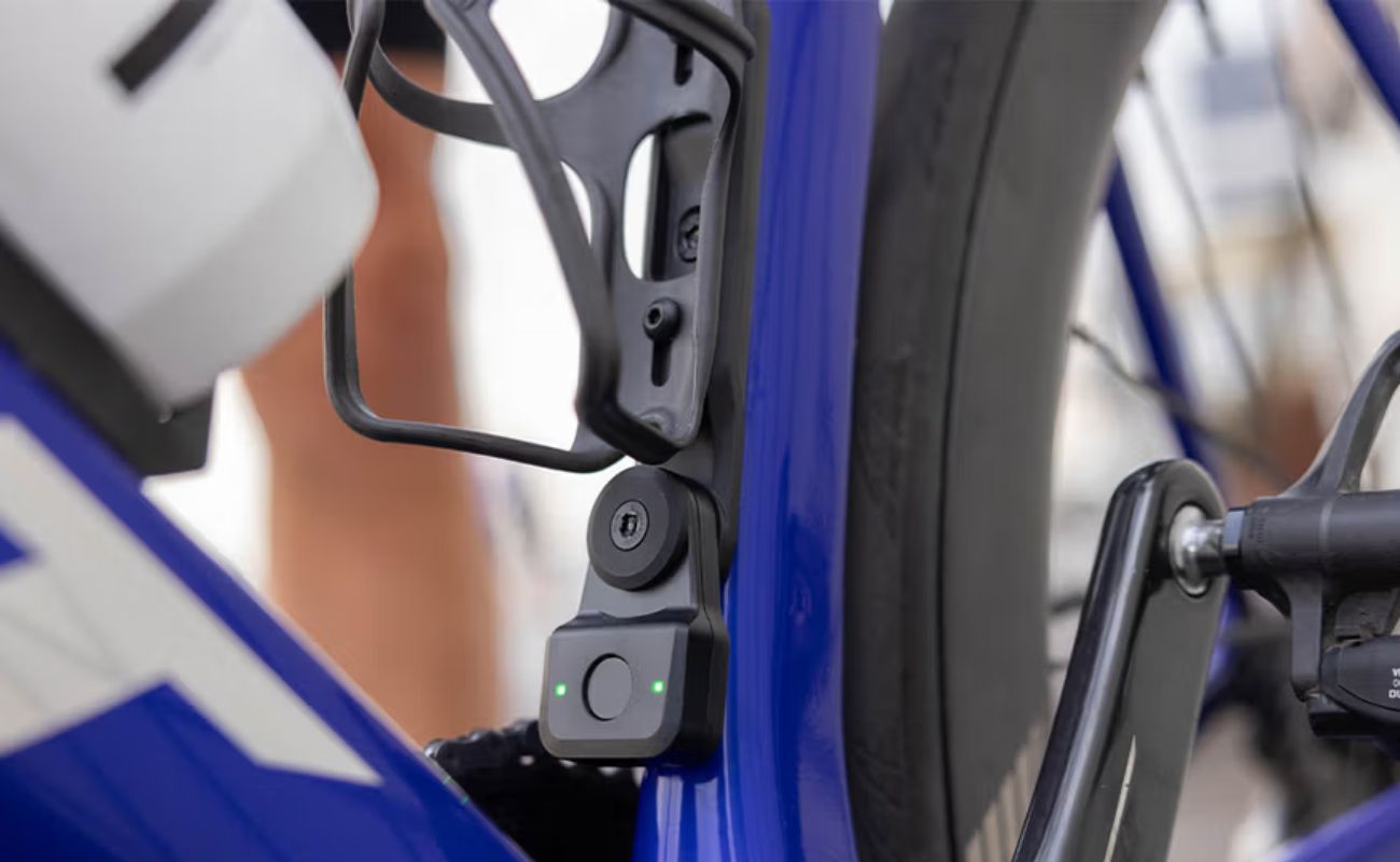 Close-up of Quad Lock Bike Alarm and Finder with green indicator lights mounted below a bottle cage on a blue bike.