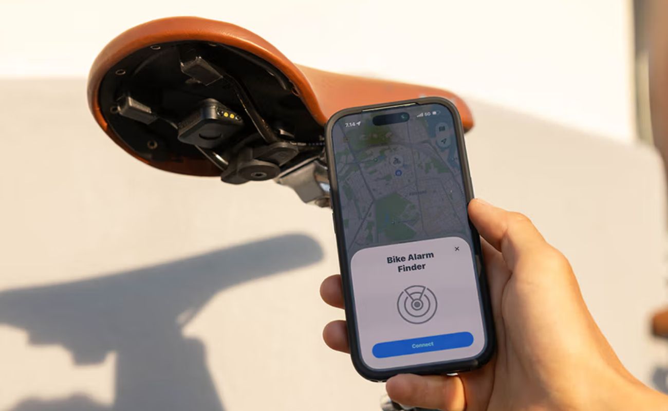 Quad Lock Bike Alarm and Finder mounted beneath a brown saddle, beside a phone showing the connection screen.