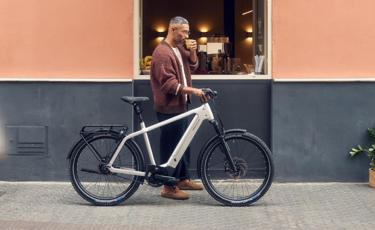 Man standing next to a Riese & Muller Charger5 Rohloff ABS EBike outside a building with a window display. | Electric Bikes Brisbane