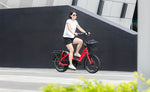 Woman riding a red Tern HSD compact electric bike with a front basket and rear cargo rack.