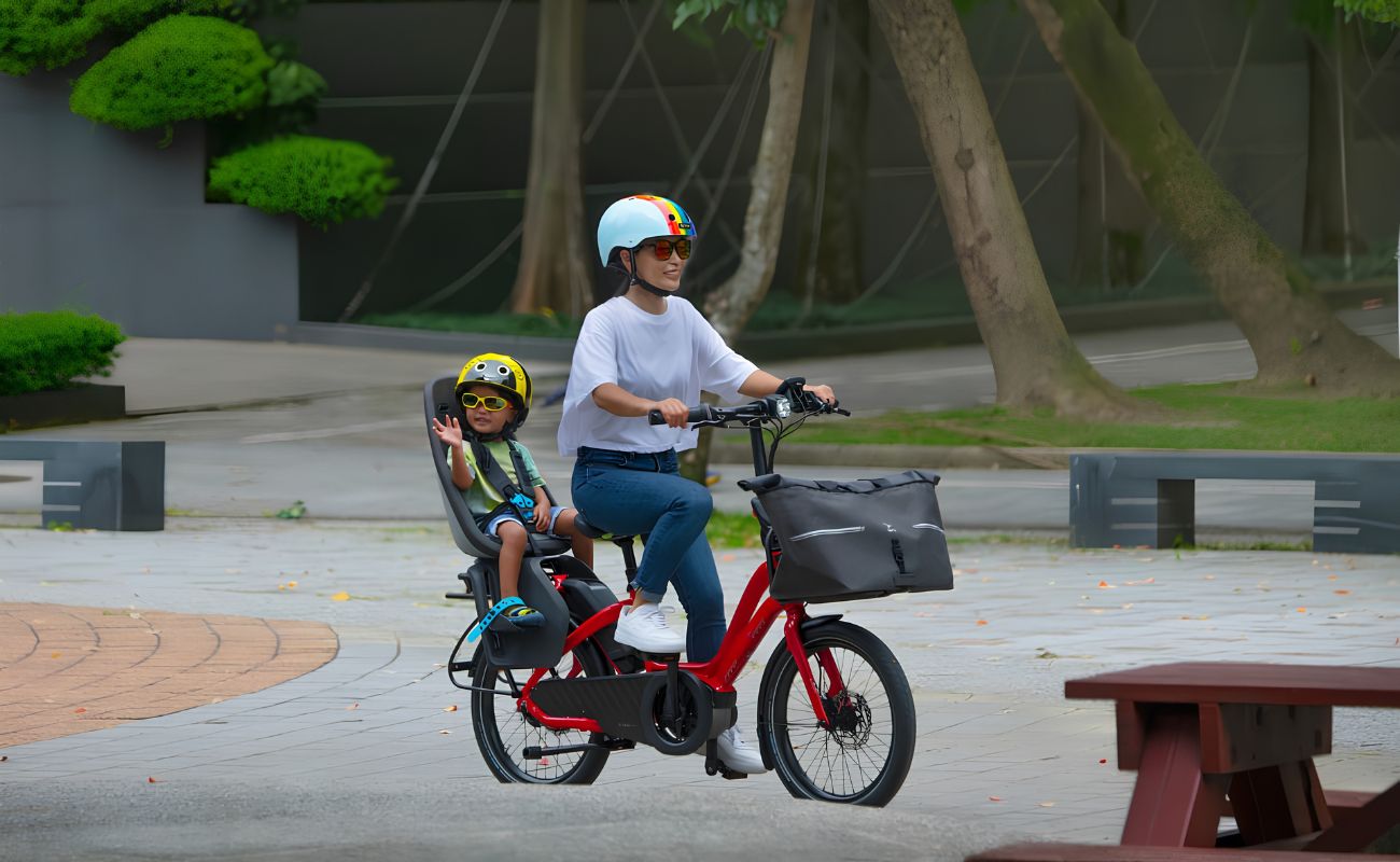 Adult riding a red Tern HSD electric bike with a child in a rear child seat and a front cargo bag.