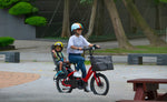 Adult riding a red Tern HSD electric bike with a child in a rear child seat and a front cargo bag.