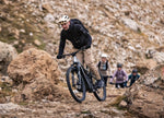 Man riding a F25 Focus Thron2 6.8 ABS electric mountain bike on a rocky path with other riders in the background.
